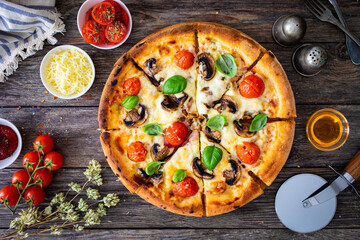 Circle vegetarian pizza with mozzarella cheese, mushrooms and tomatoes on wooden table
