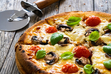 Circle vegetarian pizza with mozzarella cheese, mushrooms and tomatoes on wooden table
