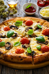 Circle vegetarian pizza with mozzarella cheese, mushrooms and tomatoes on wooden table
