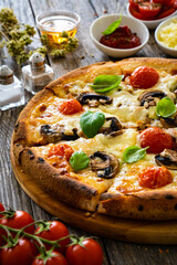 Circle vegetarian pizza with mozzarella cheese, mushrooms and tomatoes on wooden table
