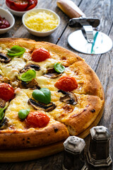 Circle vegetarian pizza with mozzarella cheese, mushrooms and tomatoes on wooden table
