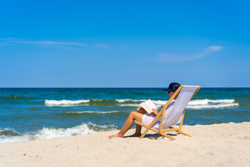 Woman relaxing on beach reading book sitting on sunbed
