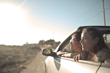 portrait of two smiling young women in a convertible car - obrazy, fototapety, plakaty