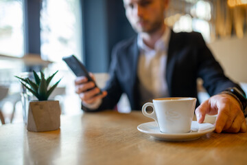 Businessman drinking morning coffee from big white cup and reading news on mobile phone