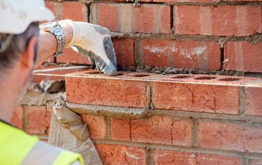 Close up of industrial bricklayer laying bricks on cement mix on construction site