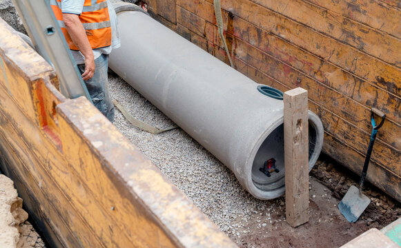 Builder installing big diameter concrete drainage pipe protected by trench support system during deep drainage works