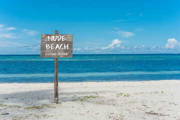 A nude beach sign posted at the beachfront. A nudist beach or naturist resort. - Powered by Adobe