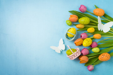 Fototapeta na wymiar Easter holiday celebration concept with easter eggs and tulip flowers on blue background. Top view, flat lay