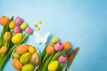 Easter holiday celebration concept with easter eggs gold flatware and tulip flowers on blue background. Top view, flat lay