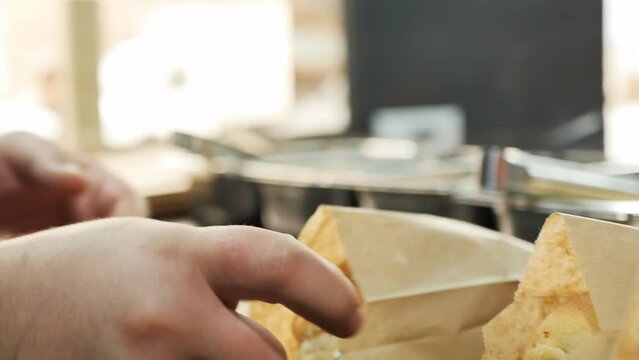 The hand of a fast food chef puts a bun with meat and vegetables inside a paper food bag. Chef put doner kebab from a bread roll in a package for delivery or takeaway food. Overweight due to obesity