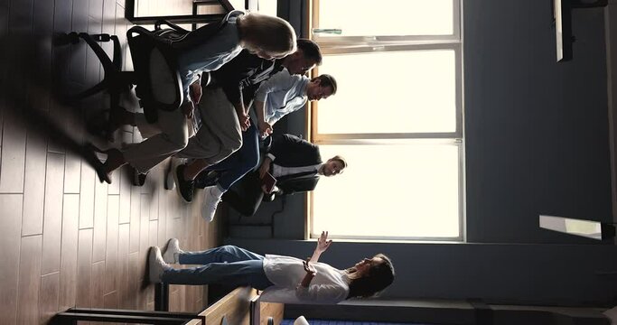 Young business woman in informal clothes presenting project to team of office colleagues, talking to coworkers, speaking, standing before audience sitting on chairs in row. Vertical shot