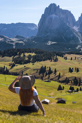 A woman in a straw hat sitting on an Alpine meadow admiring the mountain scenery. Alpe di Siusi...