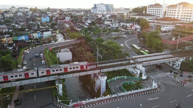 Aerial view of passenger train crossing rail bridge in near Tugu Station.