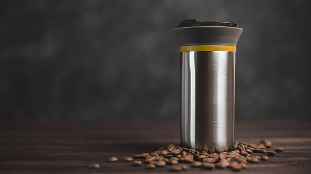 Thermos for coffee on a dark background with scattered coffee beans