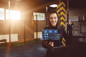 Fototapeta na wymiar Hologram of health, organism and training statistics. A woman using a hologram at the gym to check her training stats. Modern training concept