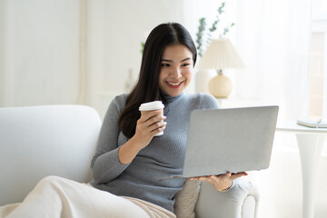 Pretty Asian woman having a relax time drinking a coffee and using laptop.