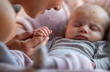 Cute newborn baby holding mother's hand while sleeping