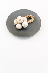 immagine con piatto in porcellana scuro e treccia d'aglio su superficie bianca