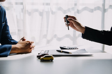 Naklejka premium A car rental company employee is handing out the car keys to the renter after discussing the rental details and conditions together with the renter signing a car rental agreement. Concept car rental.