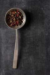 Big old spoon with peppercorn on black background