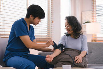 A health visitor is measuring blood pressure a sick elderly woman who is sitting on a sofa at home. This scene illustrates the concept of home health care services.