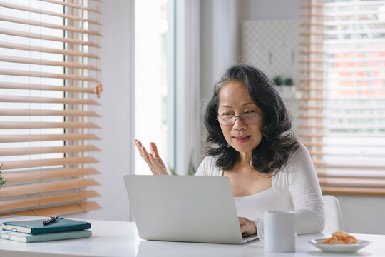 A beautiful Senior businesswoman entrepreneur is using a laptop computer to meeting conference with colleagues discuss project planning, offer advice on financial data report at her home office.