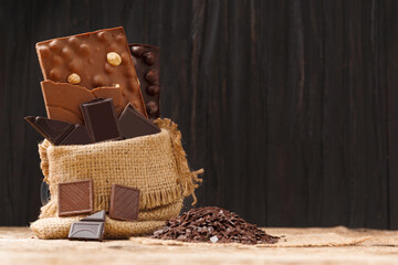 Chocolate in a burlap bag, chocolate chips on a wooden background.