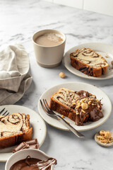 Slice of brioche babka bread with chocolate filling on white marble background served with chocolate and nuts. Easter traditional baking