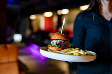 woman waiter holding plate with burger and French fries at cafe