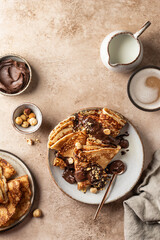 Crepes with chocolate and hazelnuts on beige background. Thin pancakes as delisious breakfast or dessert concept, Pancake day, Maslenitsa. Top view