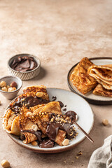 Crepes with chocolate and hazelnuts on beige background. Thin pancakes as delisious breakfast or dessert concept, Pancake day, Maslenitsa. Copy space