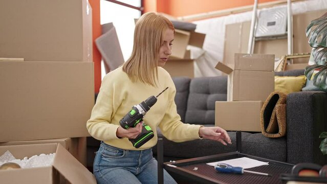 Young blonde woman holding drill sitting on floor at new home