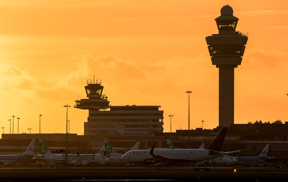 Various airline carriers on the ground at Amsterdam Schiphol International Airport during sunset.