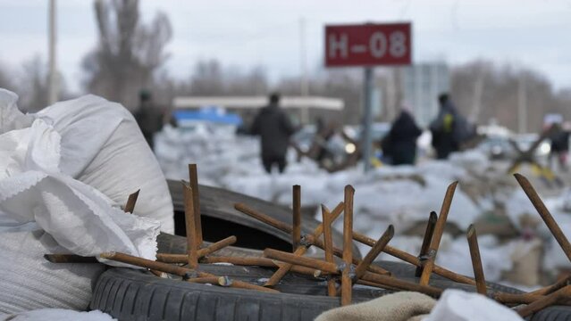 A close plan of home -made metal spikes lying on a barrekad, consisting of bags of sand and old car tires. Behind a blurry view of the block post. Russian-Ukrainian war.