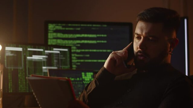 Hacker tells his requirements on the phone. Programmer talking on the phone while coding in the office. IT specialist's work routine. Software developer calling someone