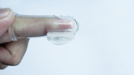 A hand wearing baby tooth brush or infant tooth brush, helping the first teeth clean isolated on white some negative space.