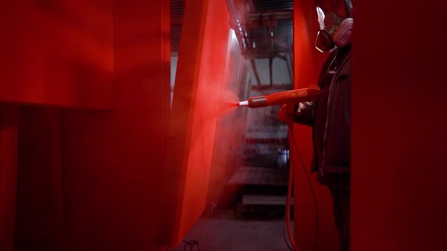a worker in a factory paints metal with red paint in a gas mask and a respirator close-up