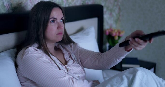 The girl lying on the bed switches the channel using the remote control. 