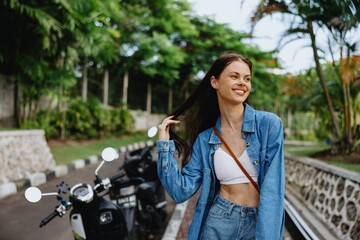 Fototapeta na wymiar Portrait of a woman brunette smile with teeth walking outside against a backdrop of palm trees in the tropics, summer vacations and outdoor recreation, the carefree lifestyle of a freelance student.