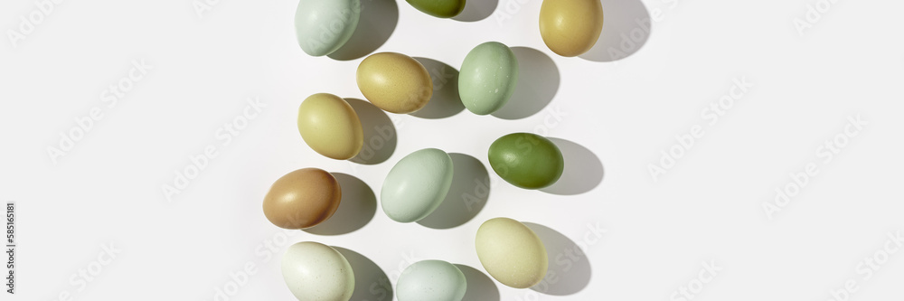 Wall mural Natural colorful Easter eggs green beige yellow color on white light background, hard Shadow at sunlight. Minimal flat lay from Chicken eggs, traditional Easter holiday food, top view