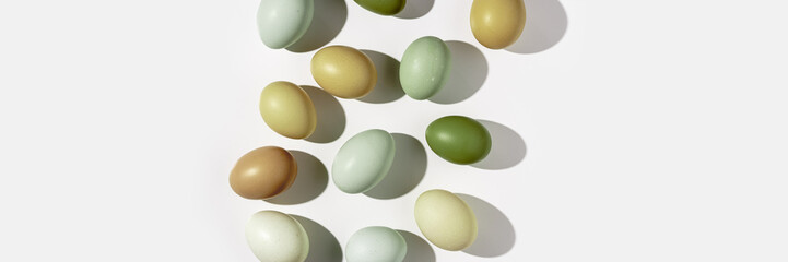 Natural colorful Easter eggs green beige yellow color on white light background, hard Shadow at sunlight. Minimal flat lay from Chicken eggs, traditional Easter holiday food, top view