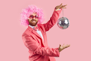 Happy cheerful man with ginger beard, wearing pink outfit, bow tie, funny curly clown wig and cool...