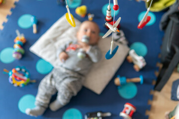 Hanging rotating wooden toy for babies. Newborn is having fun on a play mat. 