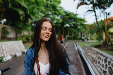 Portrait of woman brunette smile with teeth running down the street against backdrop palm trees in the tropics, summer vacations and outdoor recreation, the carefree lifestyle of a freelance student.