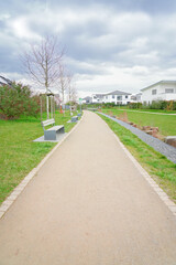 Walkway with benches in nature, park green meadow grass between quiet settlement with family houses for walks