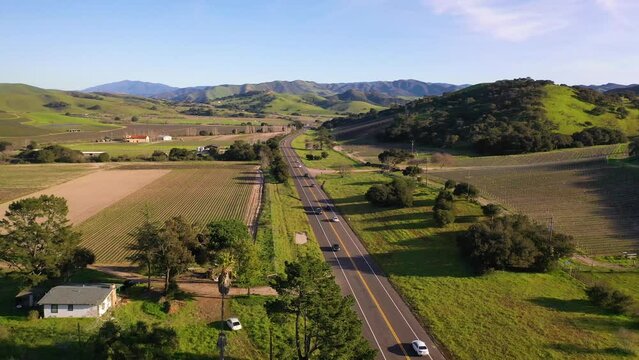 2023 - Excellent aerial footage of cars driving past farmland towards the mountains on a sunny day in Lompoc, California.