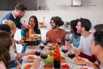 Smiling man serving spaghetti to  friends at home