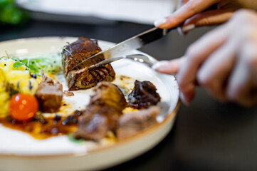 woman hands with fork and knife eating beef steak in cafe