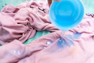 Close up of a detergent being poured on a pink sweatshirt to handwash on a traditional sink