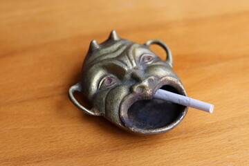 an old antique devil shaped ashtray with a cigarette in it